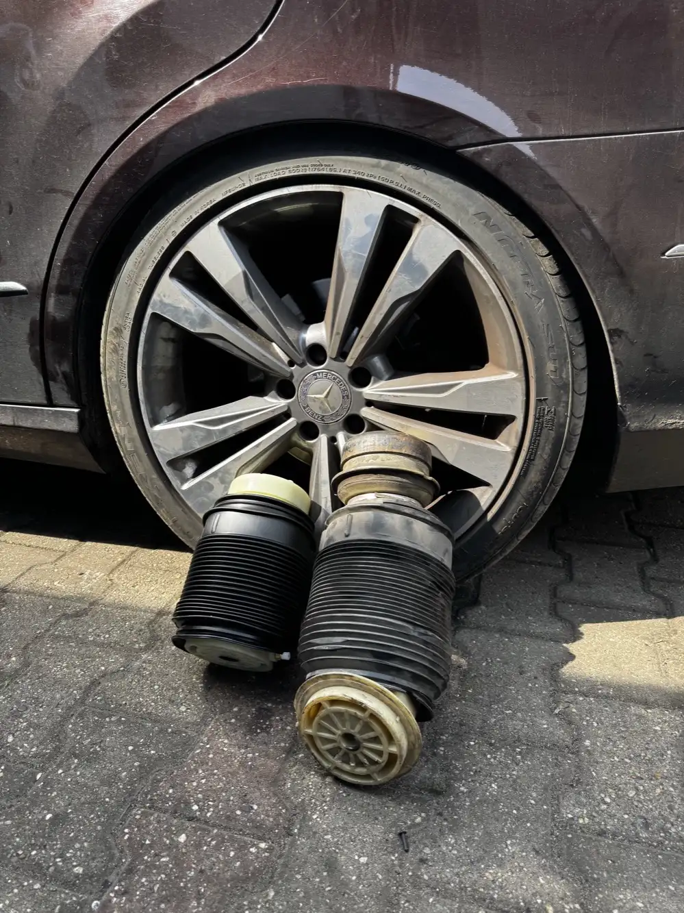 Zużyte miechy zawieszenia pneumatycznego wymontowane z Mercedesa przy kole auta